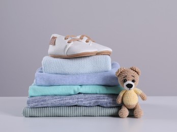 Photo of Stack of clean baby's clothes, toy and small shoes on table against light grey background. Space for text