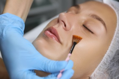 Photo of Cosmetologist applying chemical peel product on client's face in salon, closeup