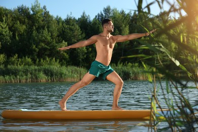 Man practicing yoga on color SUP board on river