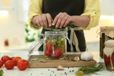 Photo of Woman putting rosemary into pickling jar at kitchen table, closeup