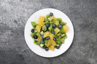 Plate of tasty fruit salad on grey textured table, top view