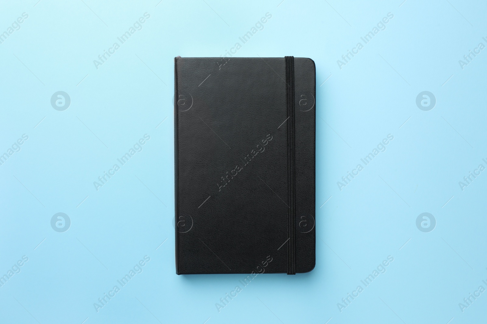 Photo of Closed black notebook on light blue background, top view