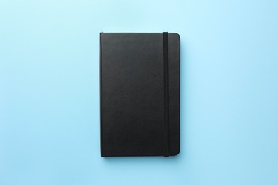 Photo of Closed black notebook on light blue background, top view