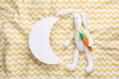 Photo of Crescent shaped child's night lamp and toy rabbit on yellow fabric, flat lay