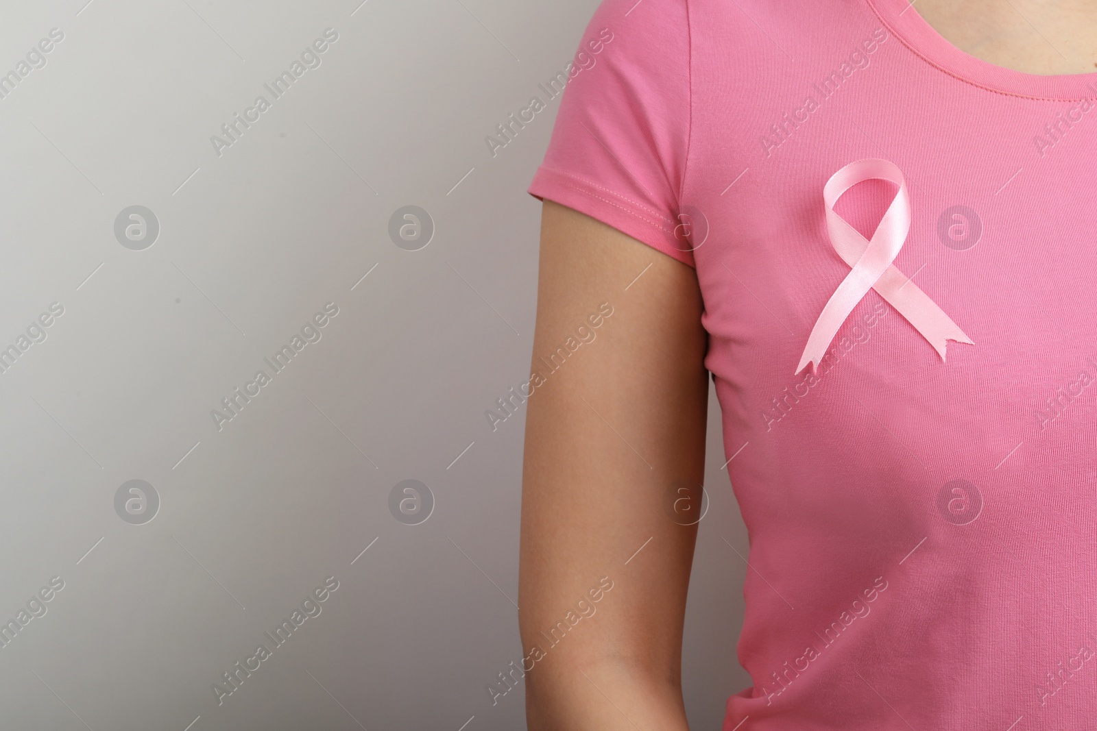 Photo of Woman with pink ribbon on grey background, space for text. Breast cancer awareness