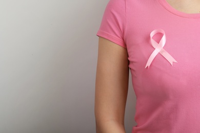 Photo of Woman with pink ribbon on grey background, space for text. Breast cancer awareness
