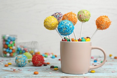 Photo of Cup with tasty cake pops on table against light background, space for text