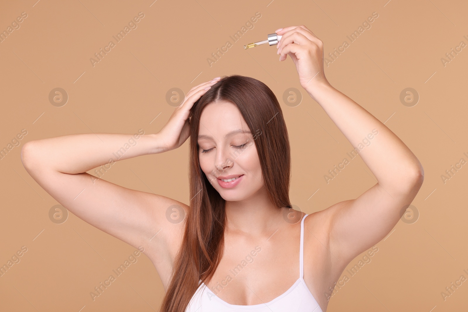 Photo of Beautiful woman applying serum onto hair on beige background