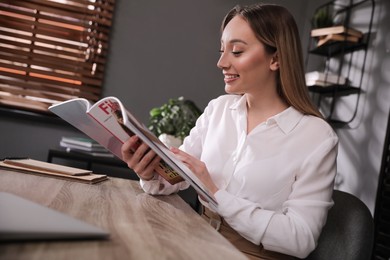 Photo of Happy woman reading magazine at workplace in office
