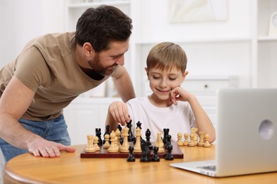 Photo of Father teaching his son to play chess following online lesson at home