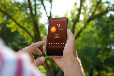 Man checking weather using app on smartphone outdoors, closeup. Data, sun and other illustrations on screen