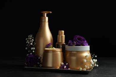 Photo of Set of hair cosmetic products and flowers on stone table against black background