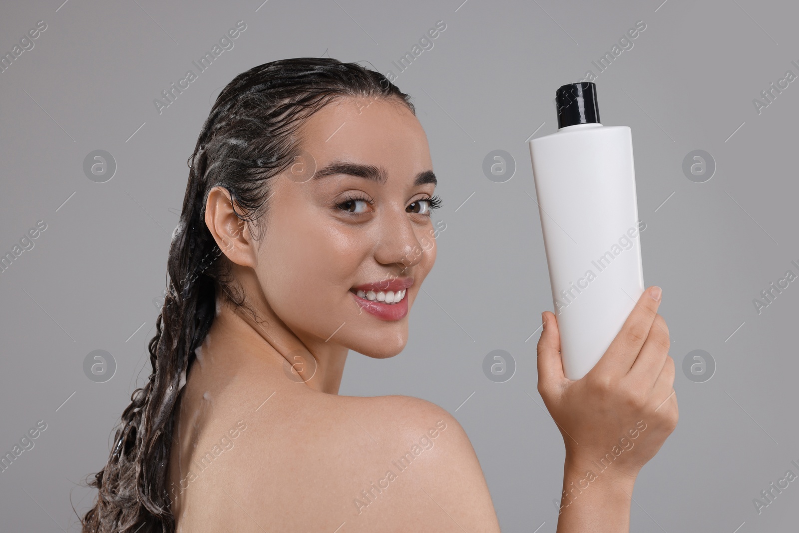 Photo of Washing hair. Portrait of beautiful happy woman with bottle on grey background