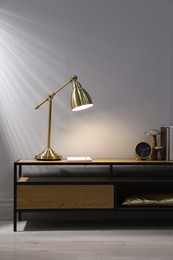 Stylish lamp, clock and books on wooden cabinet indoors. Interior design