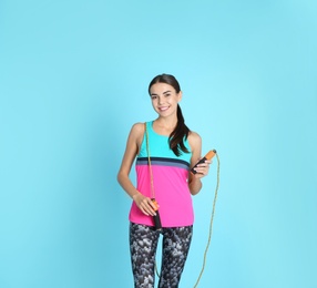 Portrait of young sportive woman with jump rope on color background