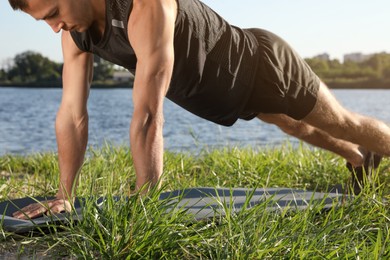 Photo of Sporty man doing straight arm plank exercise on green grass near river, closeup