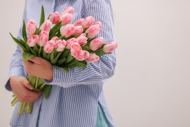 Photo of Woman with bouquet of beautiful fresh tulips on light grey background, closeup. Space for text