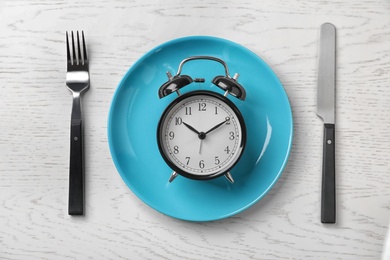 Flat lay composition with alarm clock, plate and utensils on light background