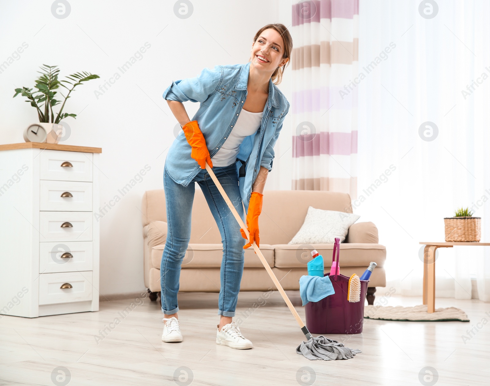 Photo of Young woman washing floor with mop in living room. Cleaning service