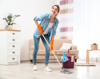 Photo of Young woman washing floor with mop in living room. Cleaning service