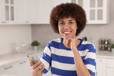Photo of Happy young woman with smartphone in kitchen