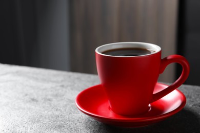 Photo of Red cup with aromatic coffee on grey textured table indoors, closeup. Space for text