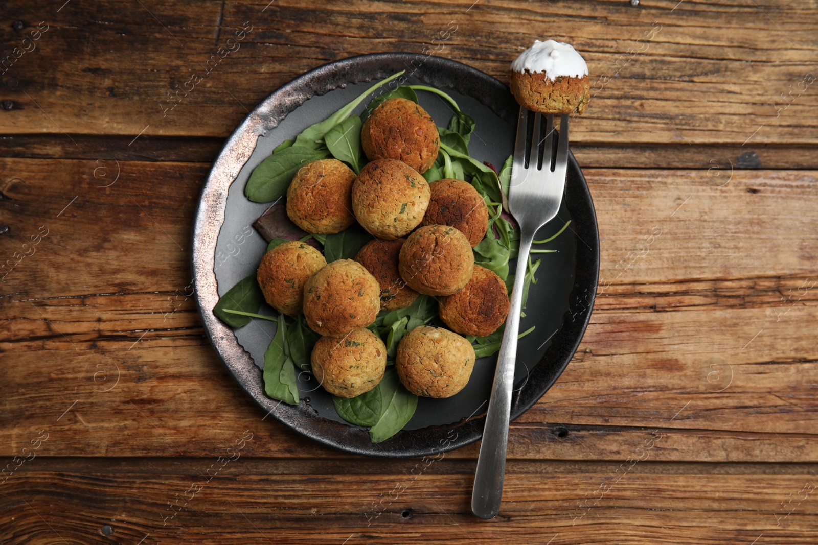 Photo of Delicious falafel balls with spinach and sauce on wooden table, top view