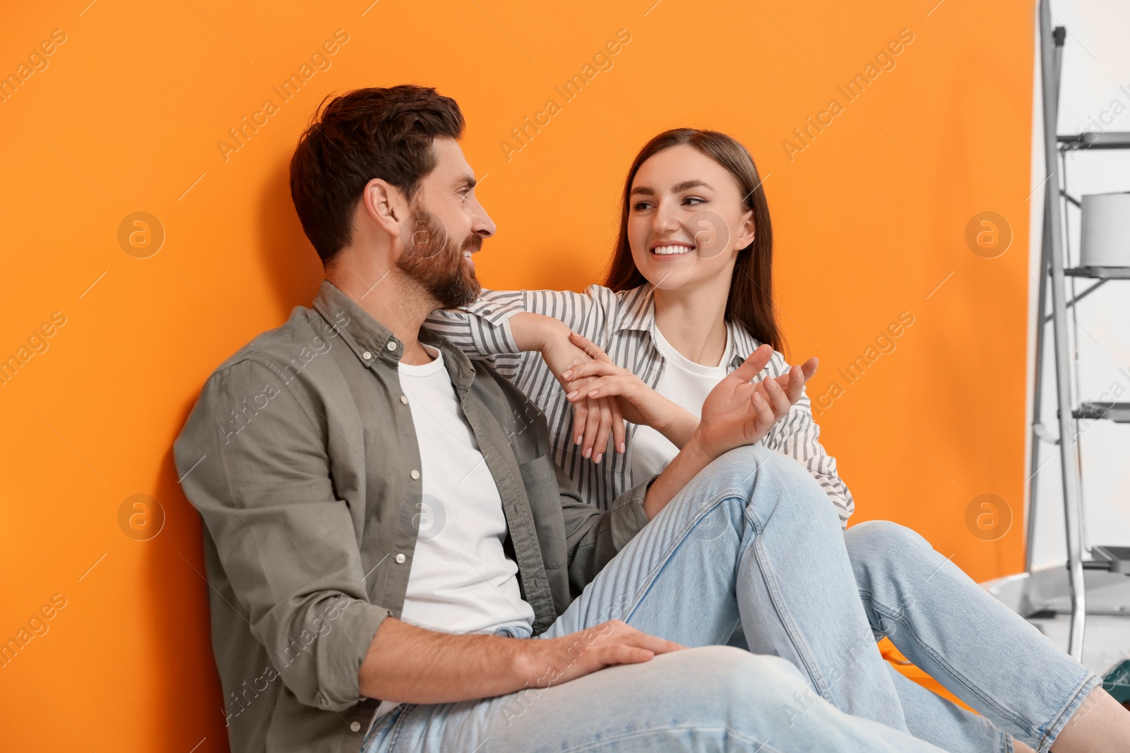 Photo of Happy designers sitting on floor near freshly painted orange wall