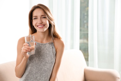 Photo of Young woman holding glass with clean water at home. Space for text