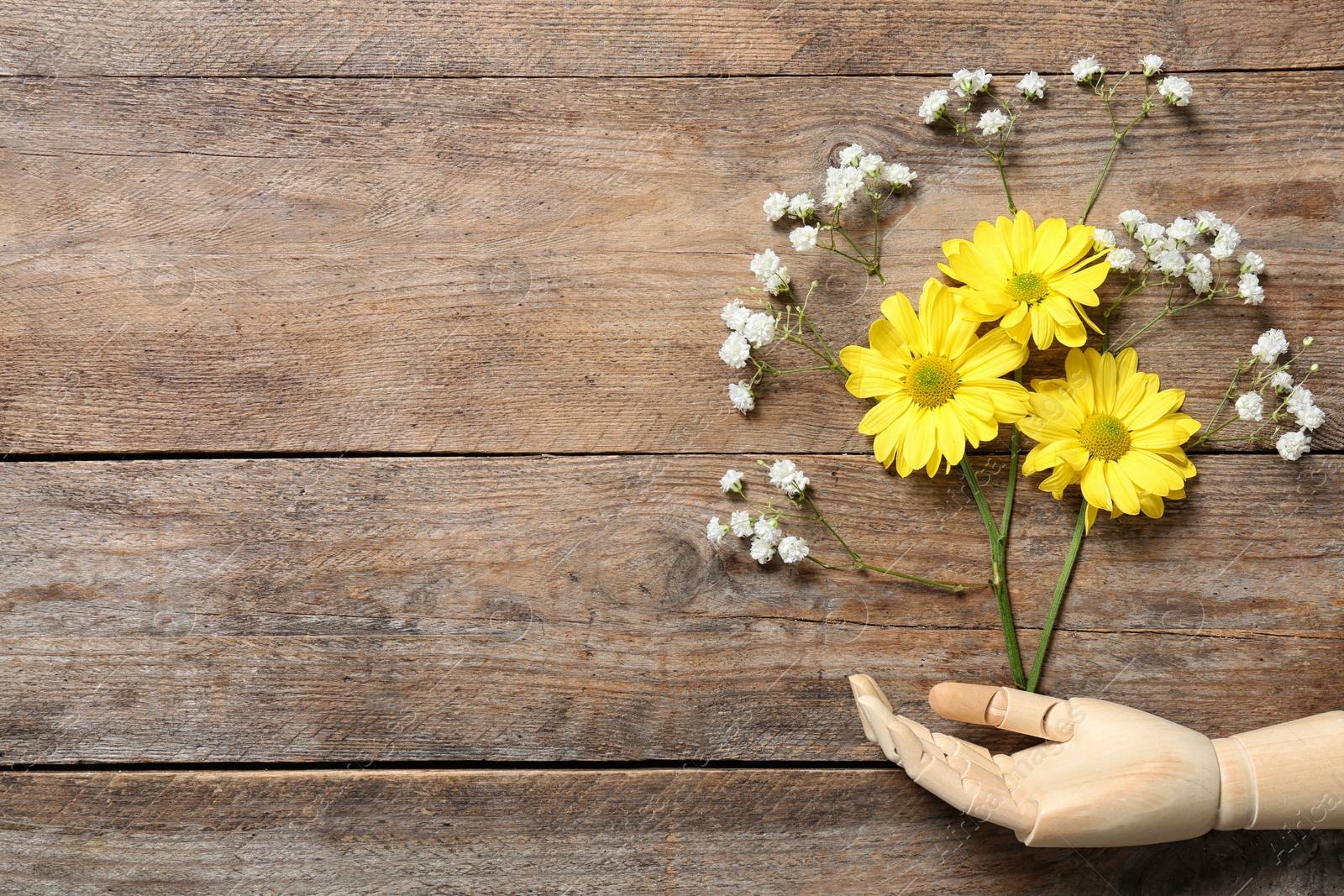 Photo of Mannequin hand and flowers on wooden background, flat lay. Space for text