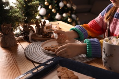 Photo of Little child decorating Christmas cookie at wooden table, closeup