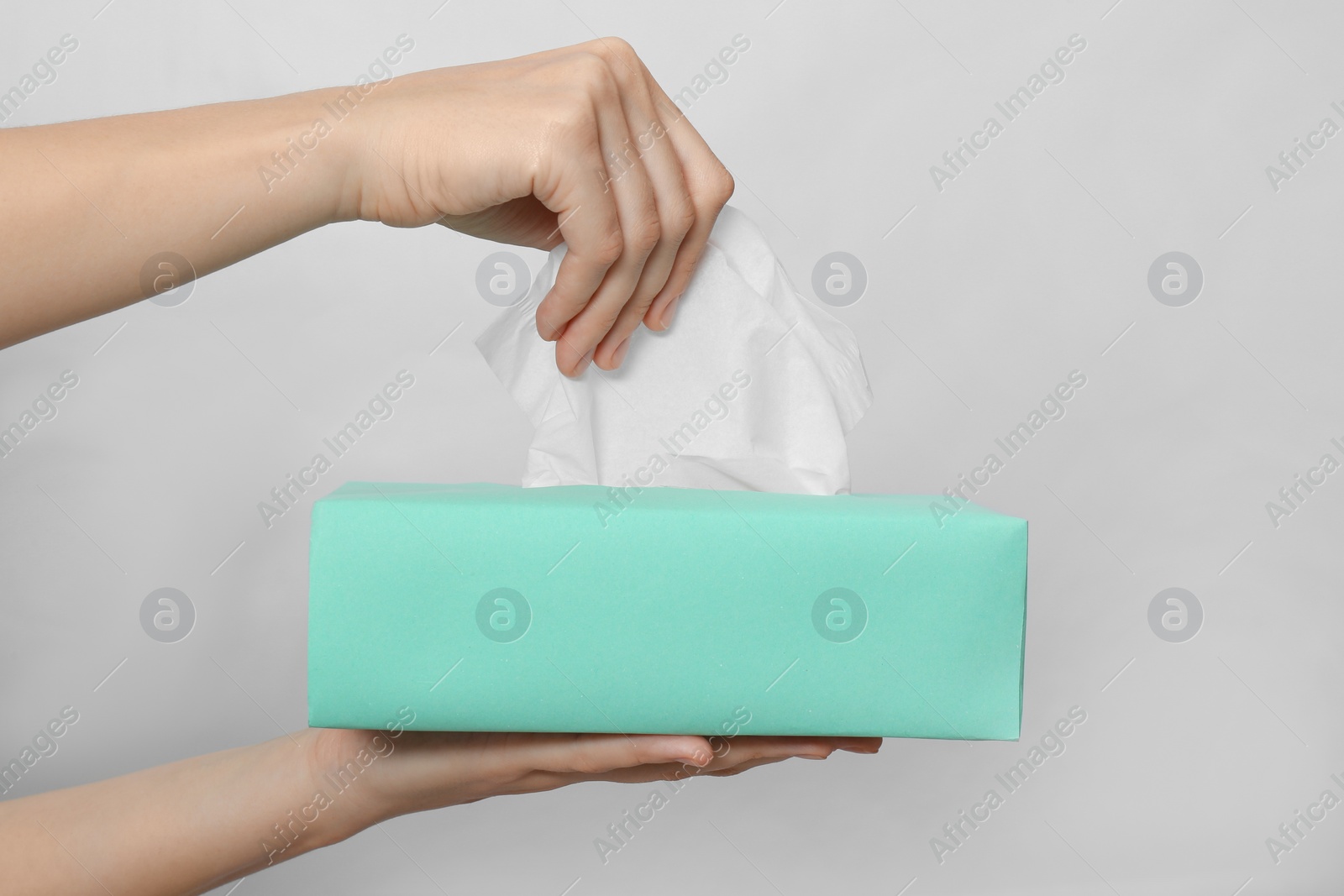 Photo of Woman taking paper tissue from box on light background, closeup