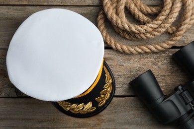 Photo of Peaked cap, rope and binoculars on wooden background, flat lay