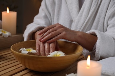 Woman soaking her hands in bowl of water and flowers at wooden table, closeup. Spa treatment