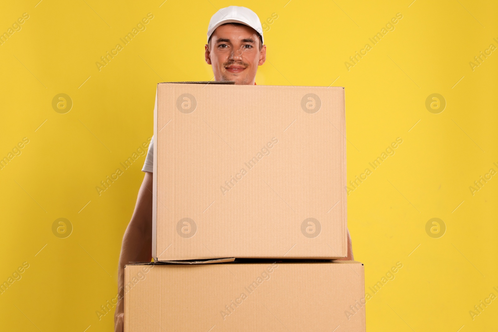 Photo of Happy young courier with cardboard boxes on yellow background