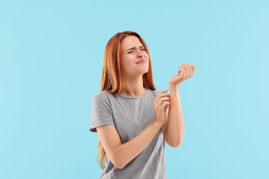 Suffering from allergy. Young woman scratching her arm on light blue background