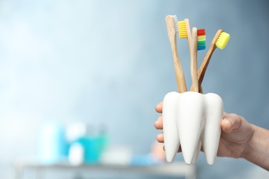 Photo of Woman with wooden toothbrushes in ceramic holder on blurred background