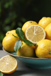 Fresh lemons and green leaves on grey table outdoors, closeup