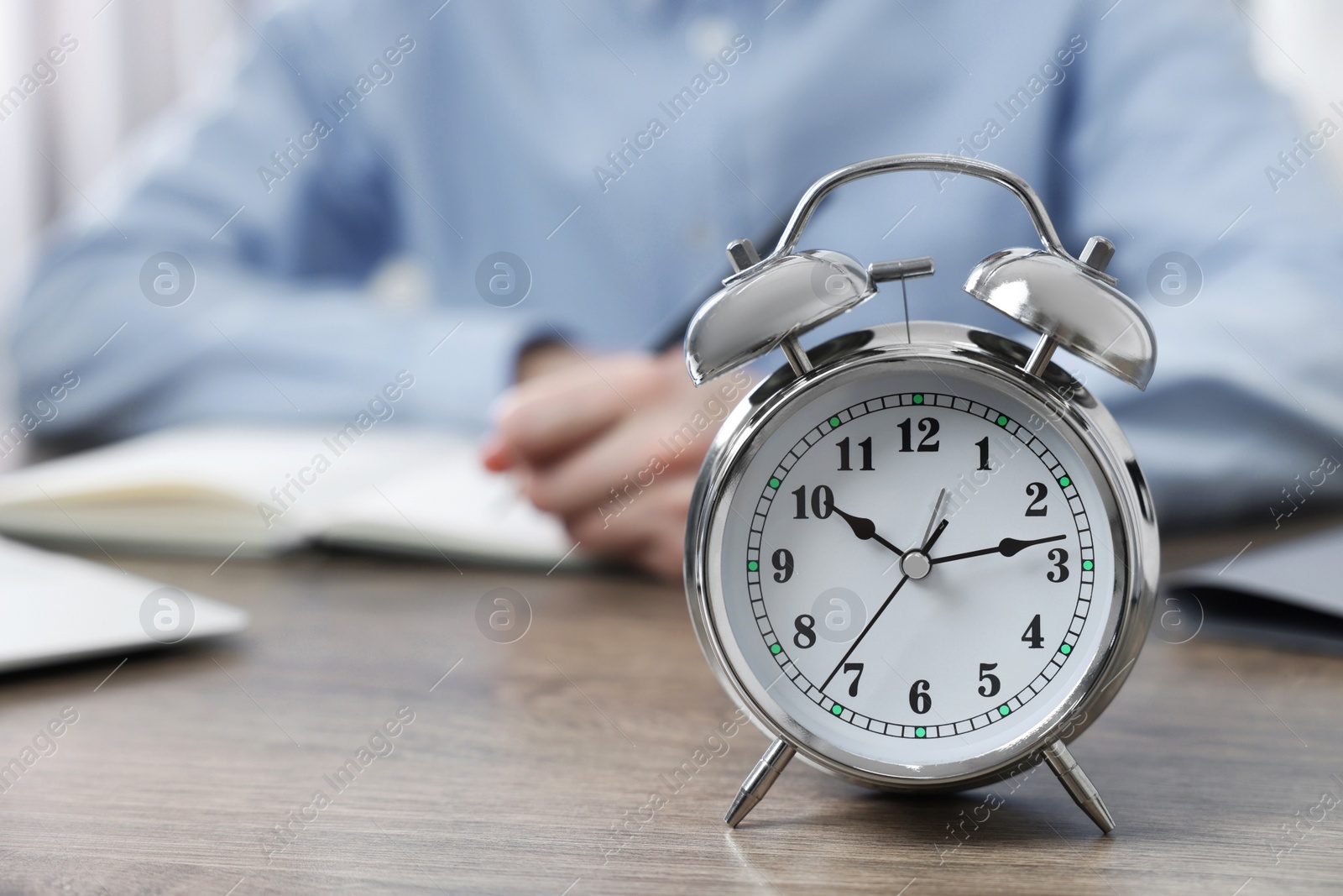 Photo of White alarm clock and man working at table, closeup. Space for text