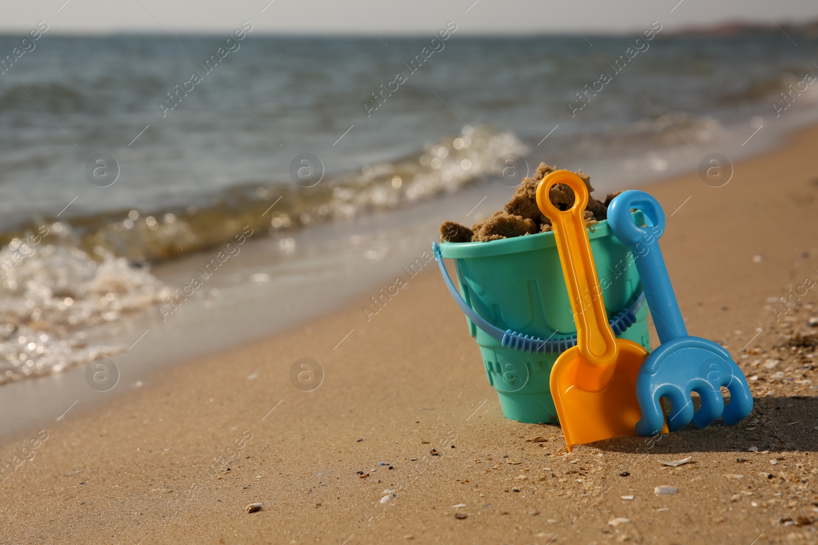 Photo of Set of plastic beach toys on sand near sea, space for text. Outdoor play