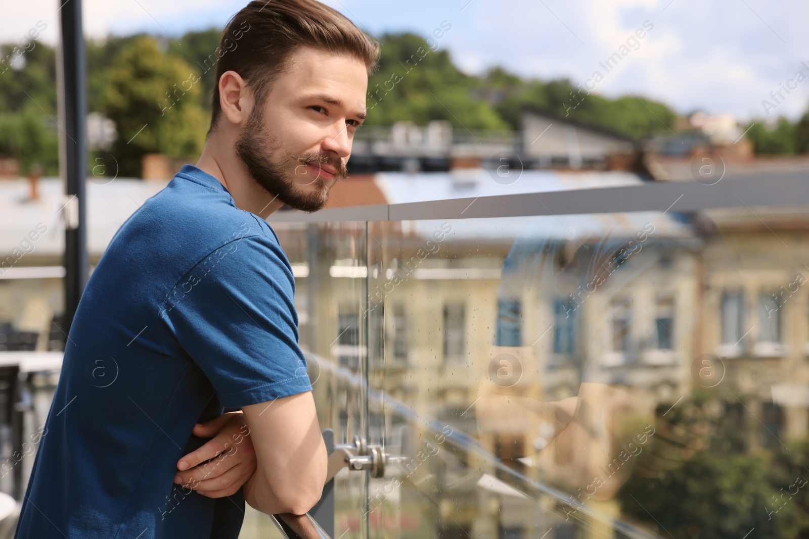 Photo of Handsome man standing on balcony in city. Space for text