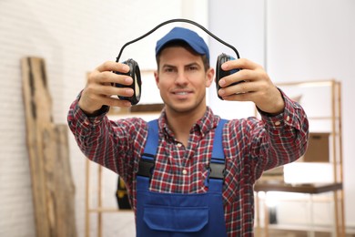 Worker holding safety headphones indoors, focus on hands. Hearing protection device