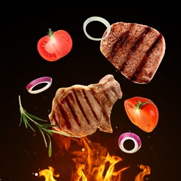 Tasty grilled meat, different vegetables and fire flame on dark background