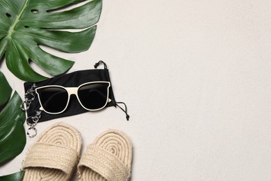 Flat lay composition with stylish sunglasses and black cloth bag on sand. Space for text