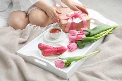 Photo of Tasty breakfast served in bed. Woman with gift box, tea, eclairs, flowers and I Love You card at home, closeup