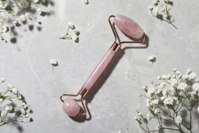 Natural face roller and flowers on grey marble background, flat lay