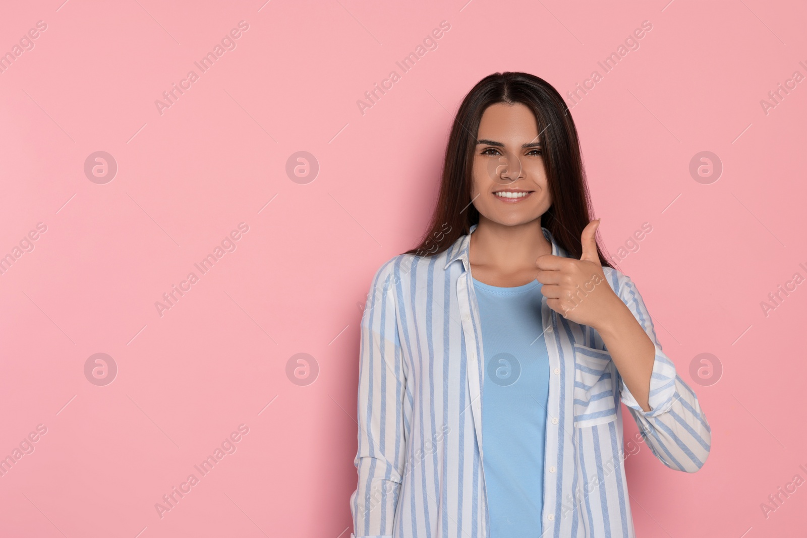 Photo of Young woman showing thumb up on pink background, space for text