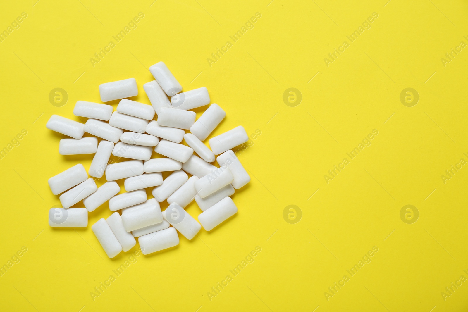 Photo of Tasty white chewing gums on yellow background, flat lay. Space for text