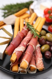 Delicious grissini sticks with prosciutto, cheese and olives on white marble table, closeup