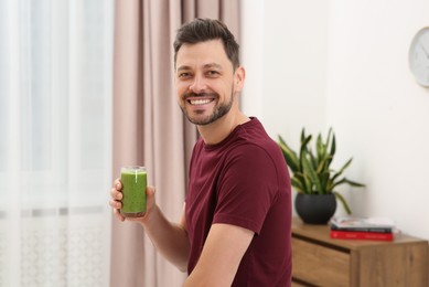 Photo of Happy man holding glass of delicious fresh smoothie at home